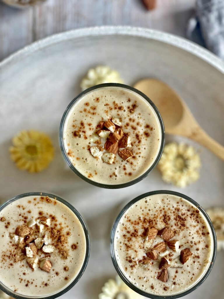 Cremiger Bananenshake mit Mandeln und Zimt in drei Gläsern auf einem Tablett.