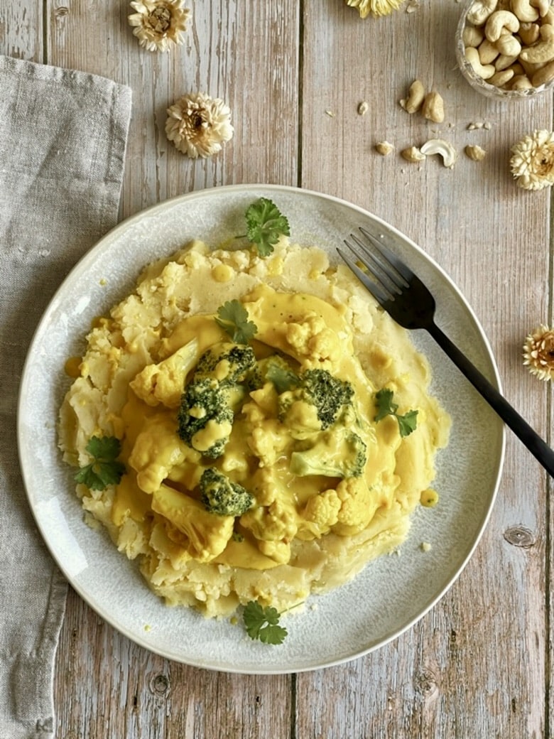 Kartoffelstampf mit Blumenkohl und Brokkoli in einer cremigen Cashewsoße auf einem Teller.