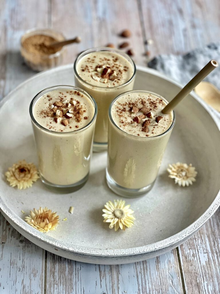 Cremiger Bananenshake mit Mandeln und Zimt in drei Gläsern auf einem Tablett.