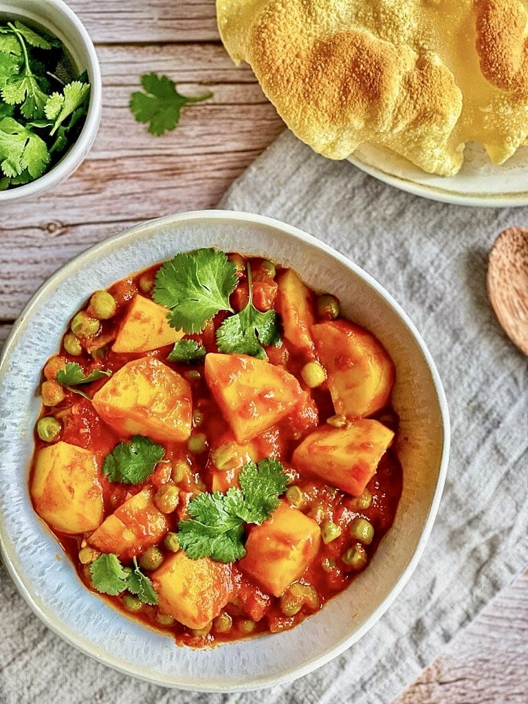 Aloo Matar: Ein veganes herzhaftes indisches Curry mit Kartoffeln und Erbsen auf einem Teller mit Naan-Brot.