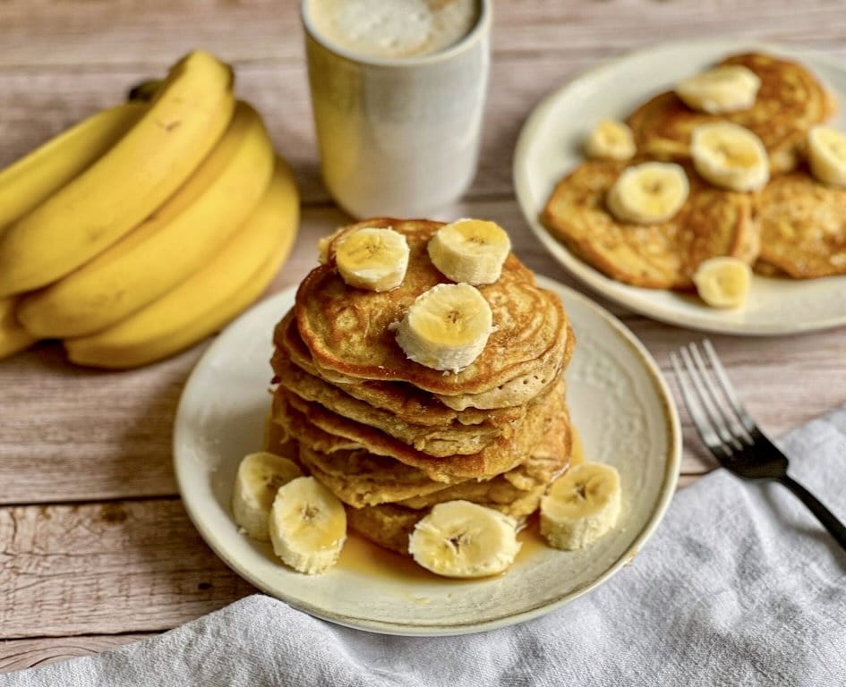 Vegane Bananen-Pancakes mit Ahornsirup gestapelt auf einem Teller.