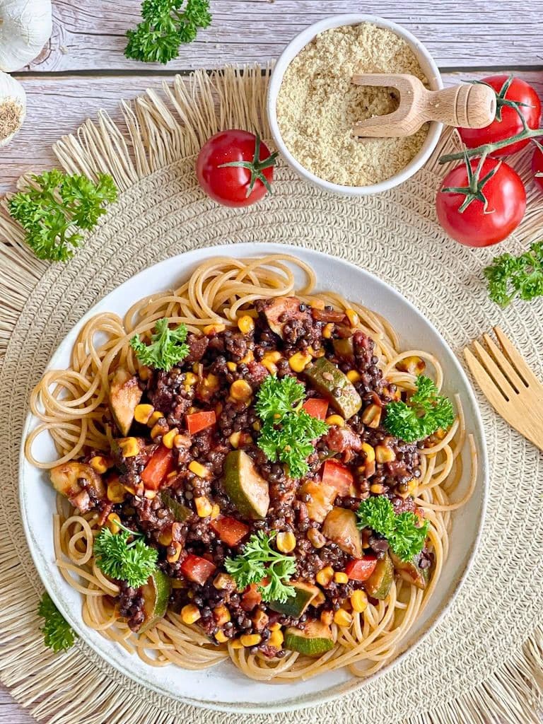 Vegane Beluga-Bolognese mit Gemüse und Spaghetti auf einem Teller.