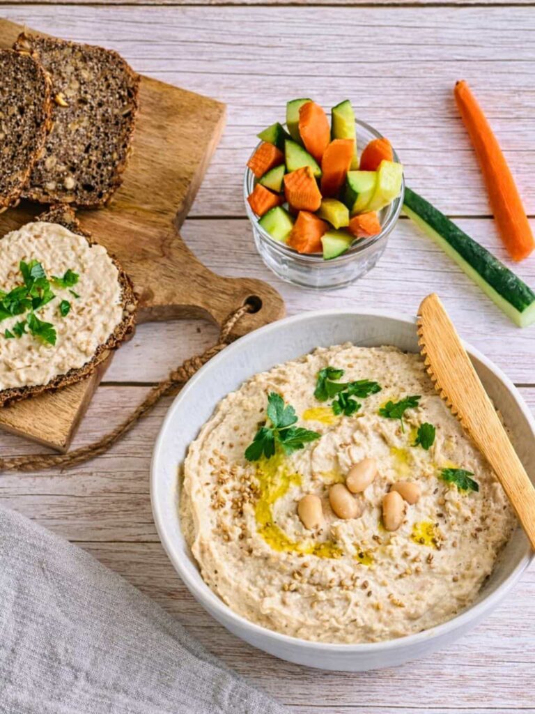 Cremiger Bohnenaufstrich in einer Schüssel mit Rohkoststicks und Vollkornbrot.