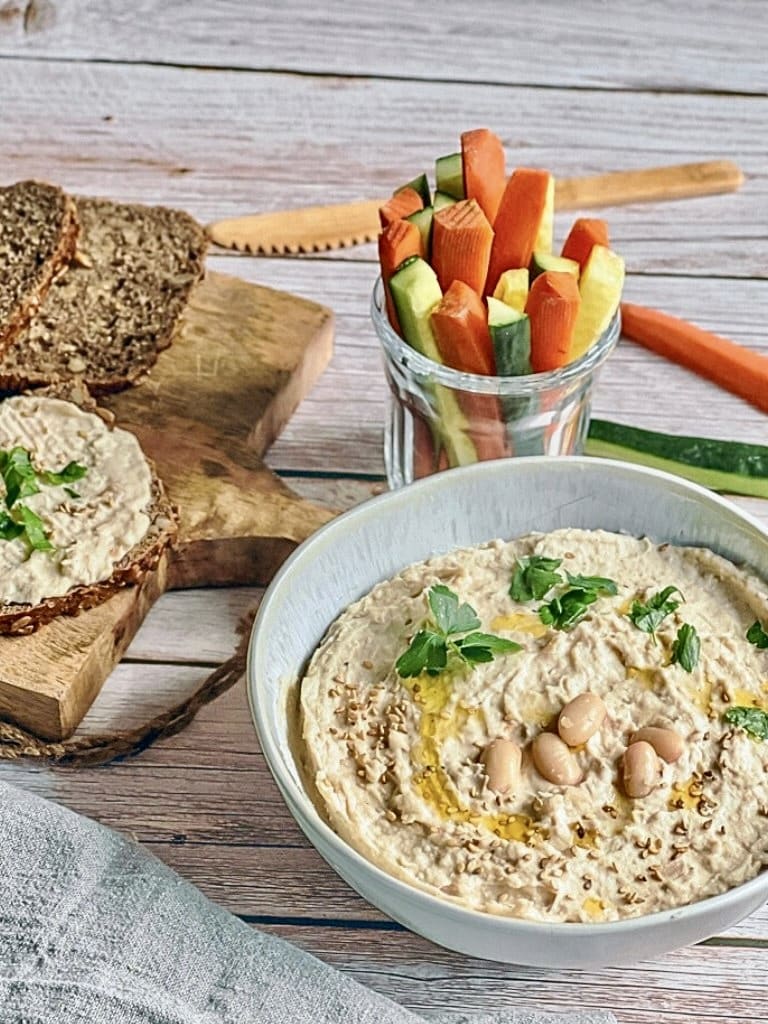 Veganer cremiger Bohnenaufstrich in einer Schüssel mit Rohkoststicks und Vollkornbrot.