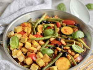 Deftige vegane Bohnenpfanne mit Räuchertofu, Tomaten und Basilikum.