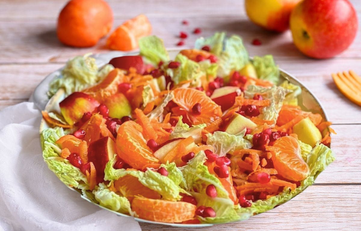 Chinakohlsalat mit Mandarinen, Äpfeln, Karotten und Granatapfelkernen in einer Schüssel