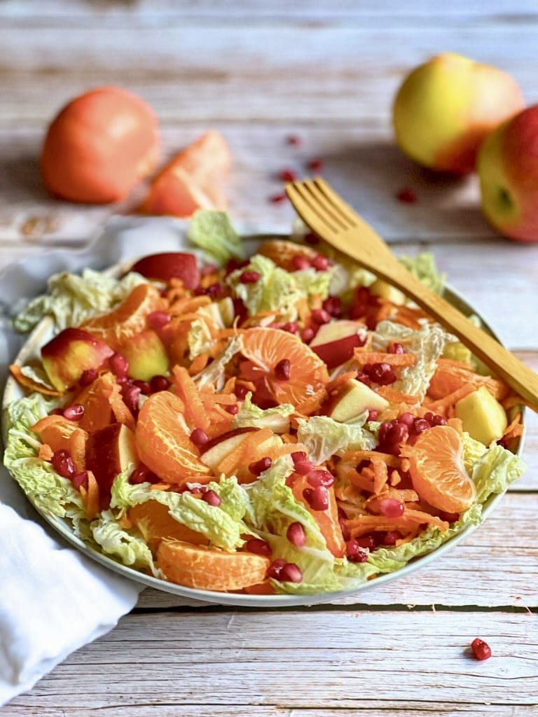 Veganer Chinakohlsalat mit Mandarinen und Apfel,, Karotten und Granatapfelkernen in einer Schüssel.