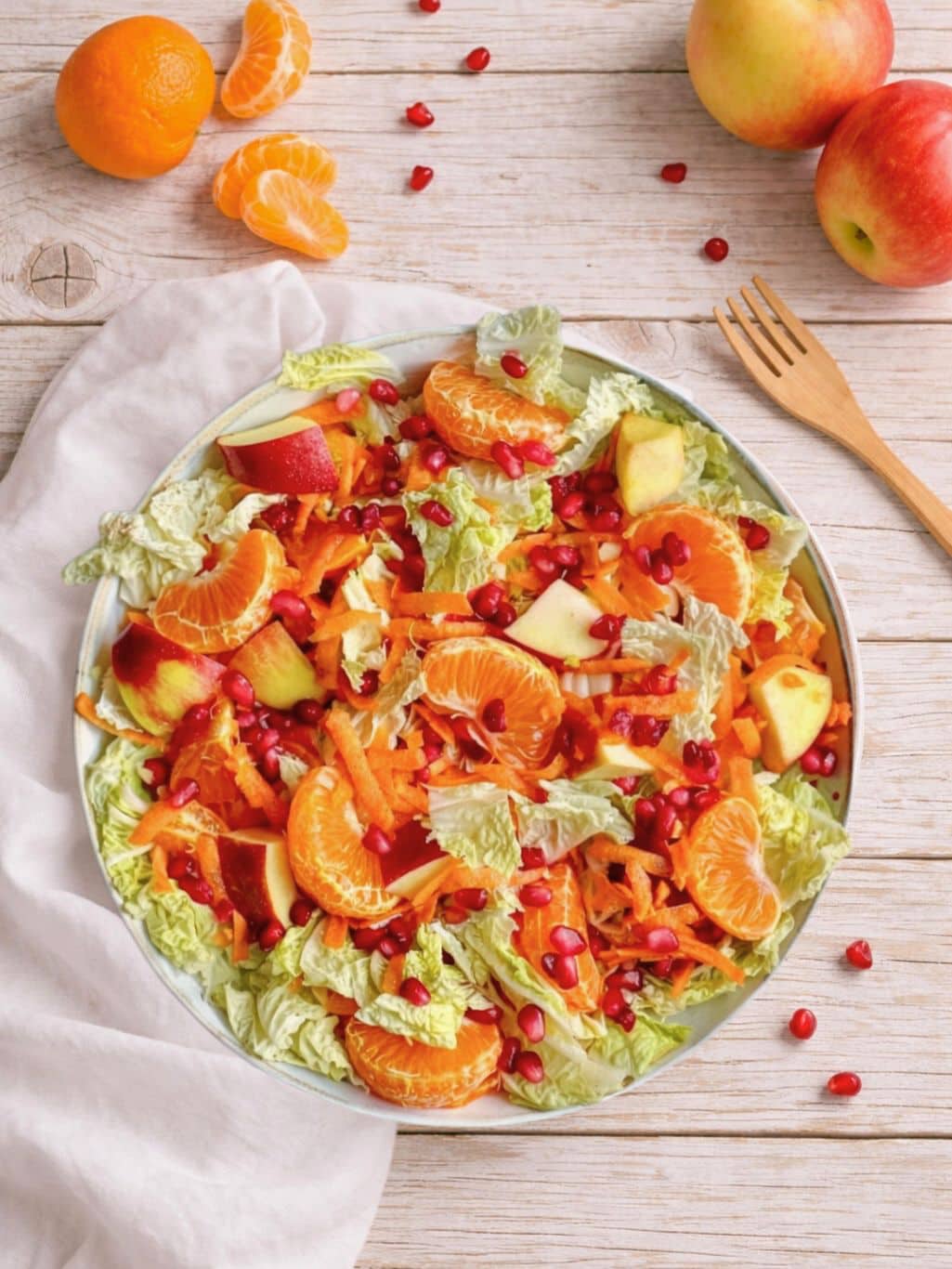 Veganer Chinakohlsalat mit Mandarinen und Apfel,, Karotten und Granatapfelkernen in einer Schüssel.