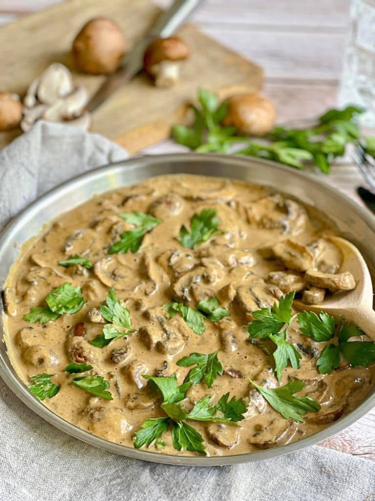 Vegane Rahmchampignons mit Petersilie in einer Pfanne auf einem Tisch.