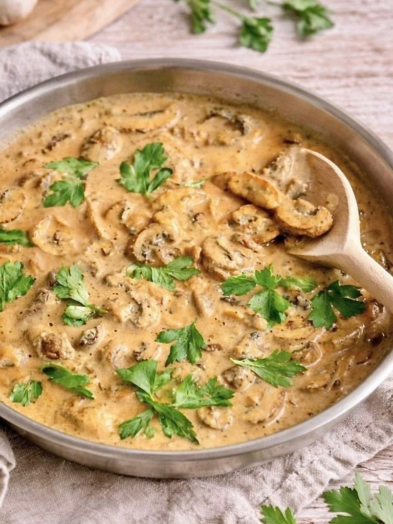 Vegane Rahmchampignons mit Petersilie in einer Pfanne auf einem Tisch.