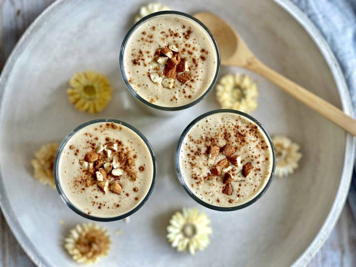 Veganer Bananenshake mit Mandeln und Zimt in drei Gläsern auf einem Tablett.