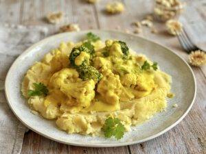 Kartoffelstampf mit Blumenkohl und Brokkoli in einer cremigen Cashewsoße auf einem Teller.