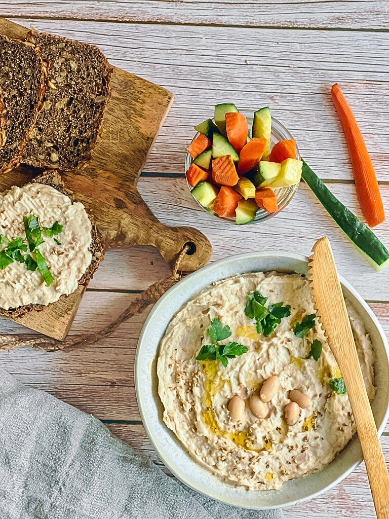 Cremiger Bohnenaufstrich in einer Schüssel mit Rohkoststicks und Vollkornbrot.