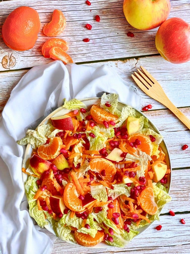 Chinakohlsalat mit Mandarinen, Äpfeln, Karotten und Granatapfelkernen in einer Schüssel