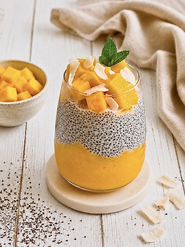 Mango-Chiapudding mit Kokos im Glas auf einem Holztisch.