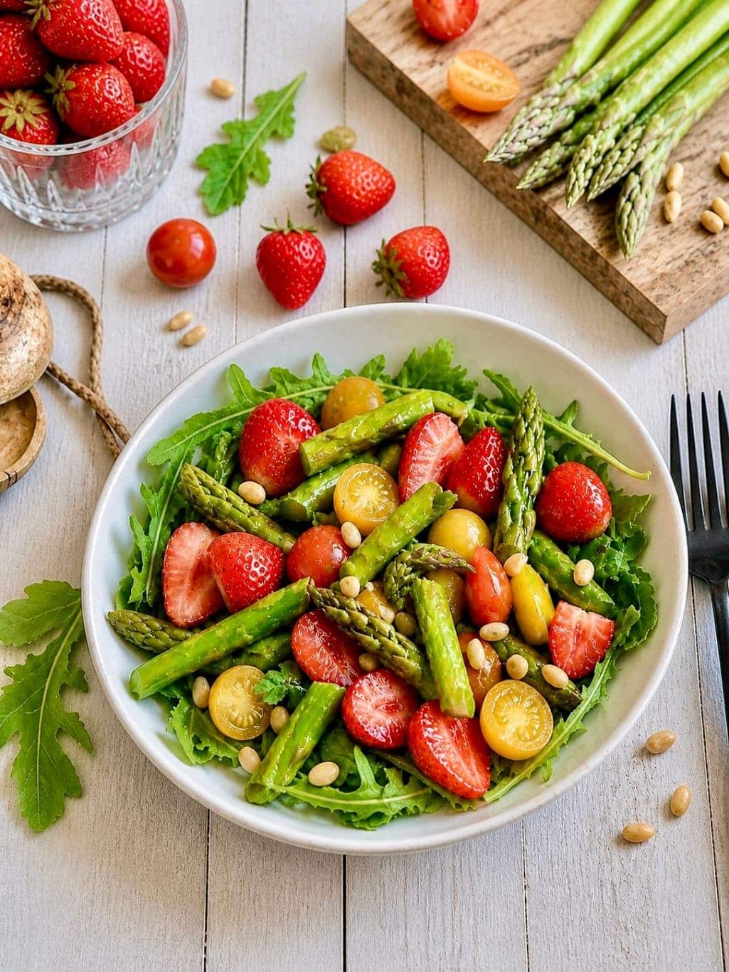 Spargelsalat mit Erdbeeren, Rucola und Pinienkerne auf einem Teller.