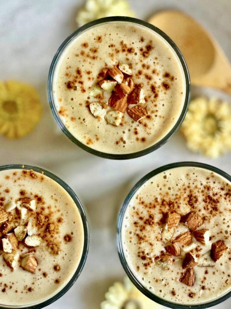 Veganer Bananenshake mit Mandeln und Zimt in drei Gläsern auf einem Tablett.