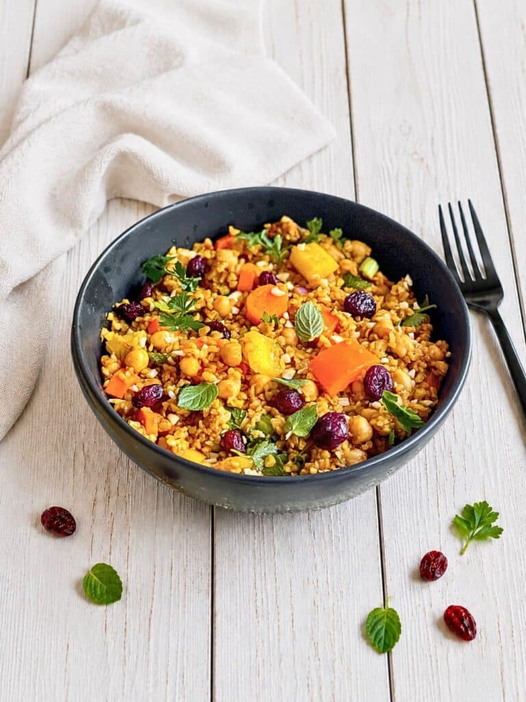 Veganer Bulgursalat mit Gemüse und Kräutern in einer Schüssel auf einem Holztisch.