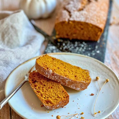 Veganer Kürbiskuchen auf einer schwarzen Platte und zwei Scheiben veganer Kürbiskuchen auf einem Teller.