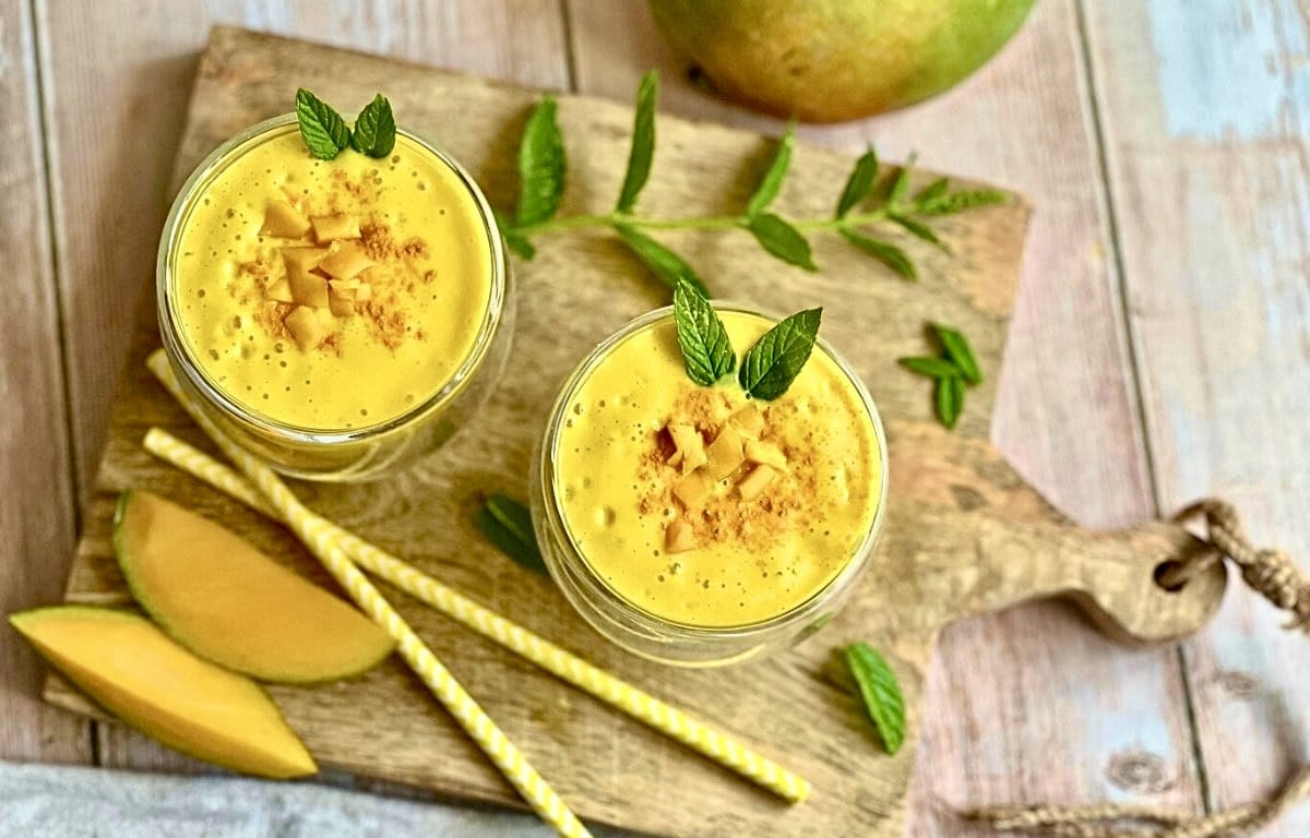Veganer Mango Lassi in 2 Gläsern auf einem Holzbrett.