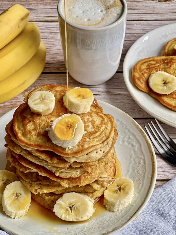 Vegane Bananen-Pancakes mit Ahornsirup gestapelt auf einem Teller.