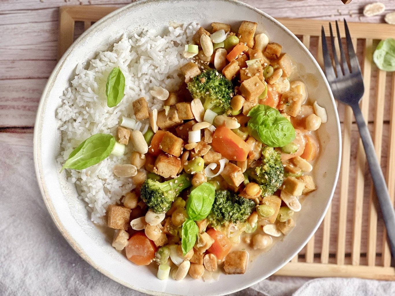 Gemüse mit Tofu in Erdnusssoße mit Reis auf einem Teller.