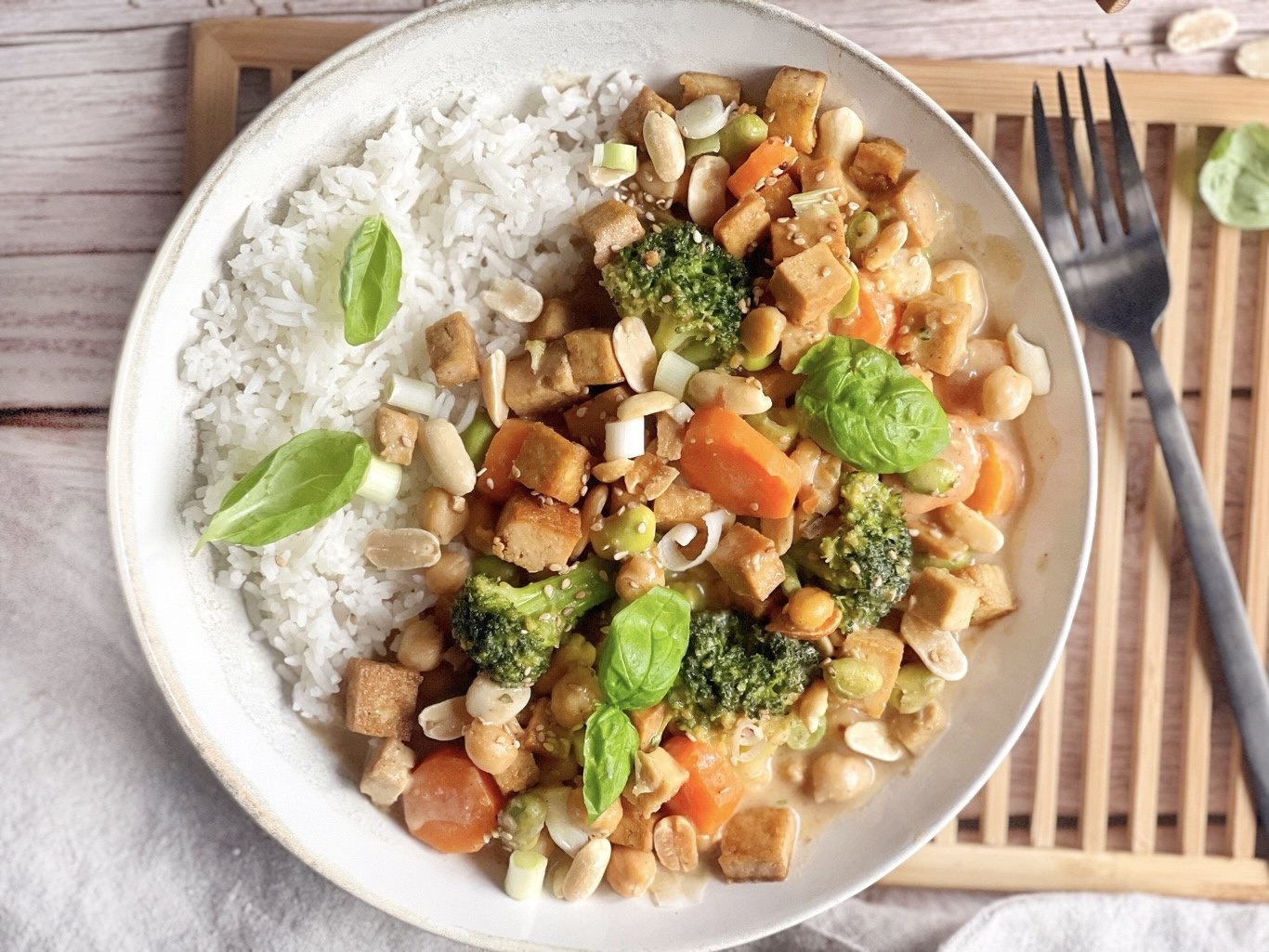 Gemüse mit Tofu in Erdnusssoße mit Reis auf einem Teller.