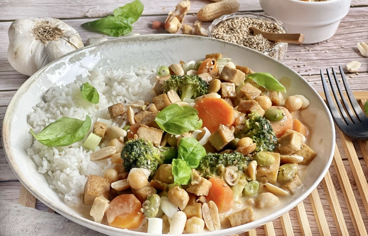 Gemüse mit Tofu in Erdnusssoße mit Reis auf einem Teller.