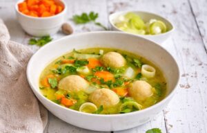 Gemüsesuppe mit veganen Grießklößchen in einem Suppenteller auf einem Holztisch.