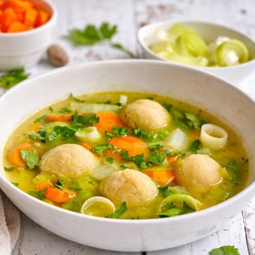 Gemüsesuppe mit veganen Grießklößchen in einem Suppenteller auf einem Holztisch.