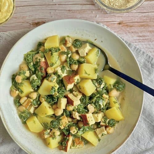 Veganer Kartoffel-Grünkohl-Eintopf mit Räuchertofu und Kichererbsen in einem Suppenteller.