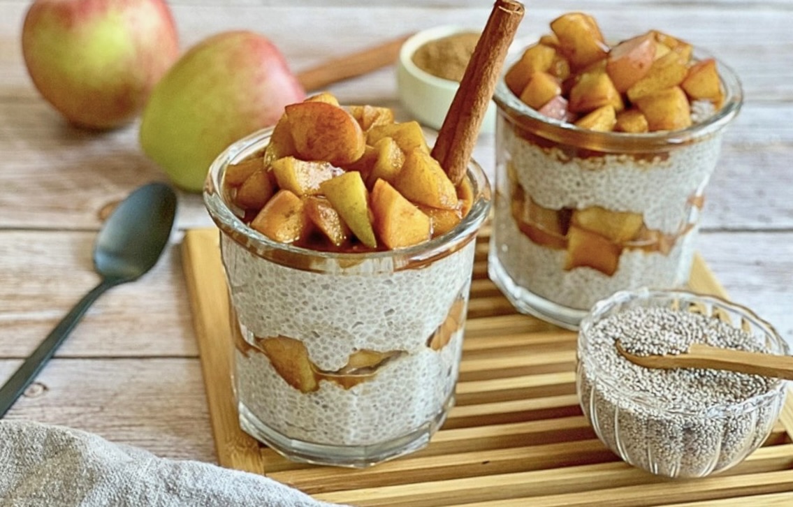 Veganer Chiapudding mit Apfel und Zimt in zwei Gläsern auf einem Holzbrett.