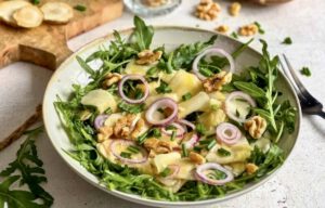 Veganer Topinambur-Salat mit Rucola und Walnüssen auf einem Teller.