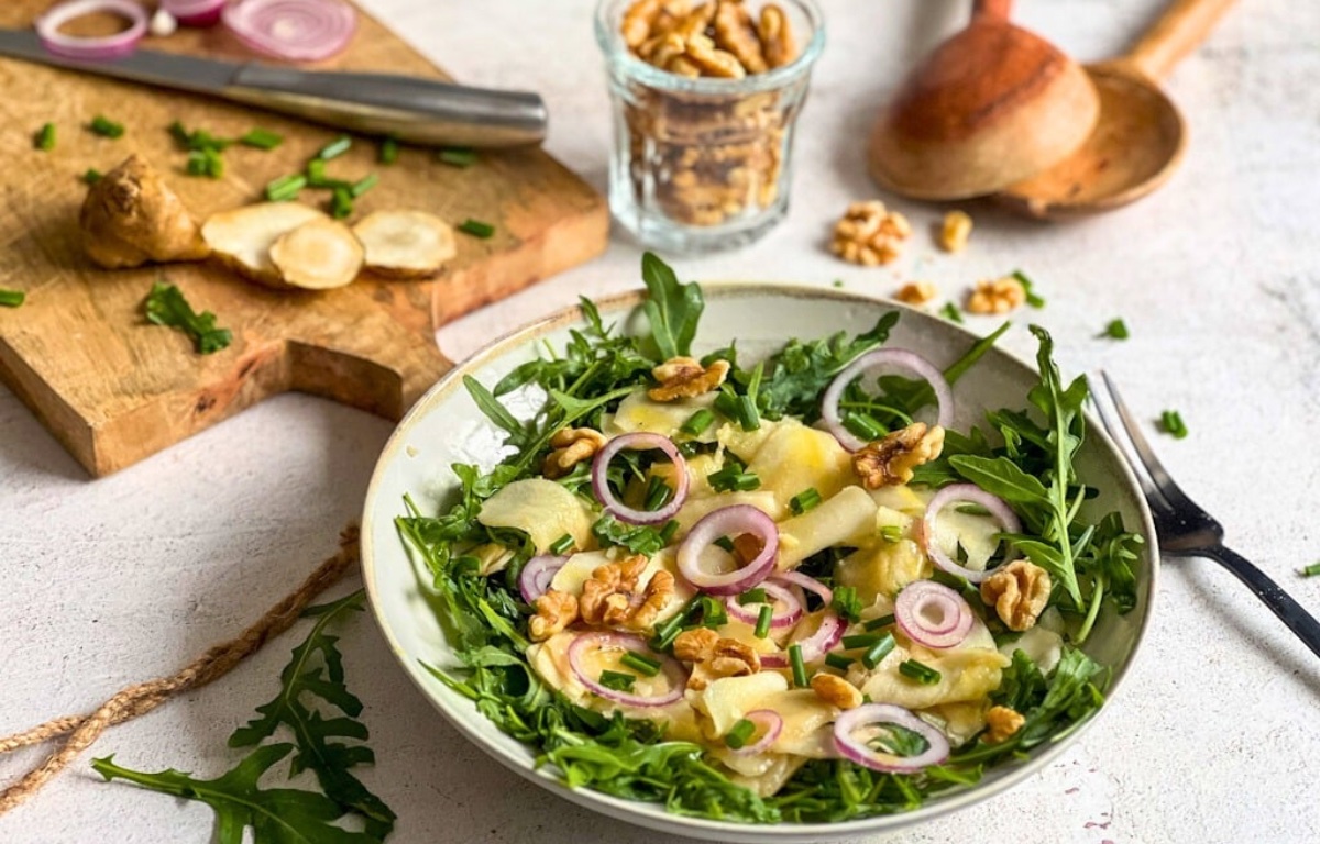 Veganer Topinambur-Salat mit Rucola und Walnüssen auf einem Teller.