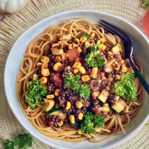 Vegane Beluga-Bolognese mit Gemüse und Spaghetti auf einem Teller.