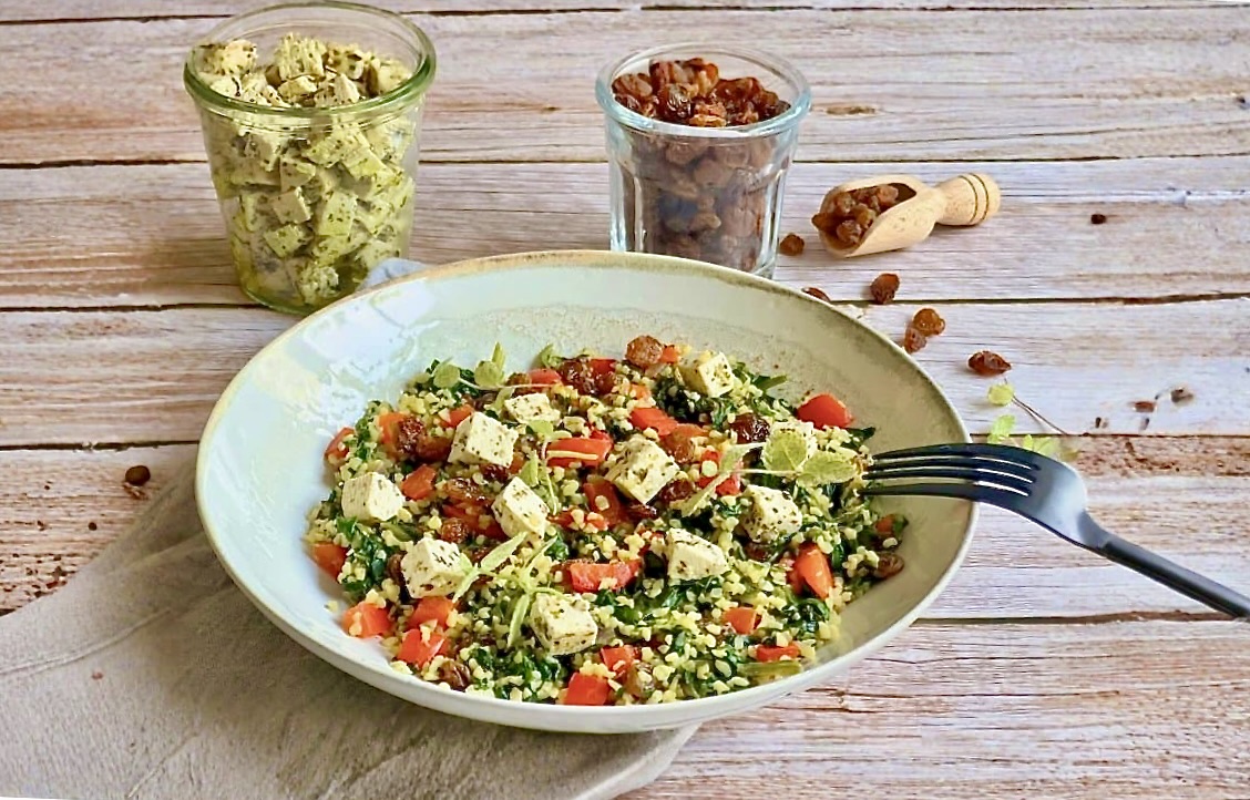 Vegane Bulgurpfanne mit Spinat, Paprika, Rosinen und Kräutertofu auf einem Teller platziert.