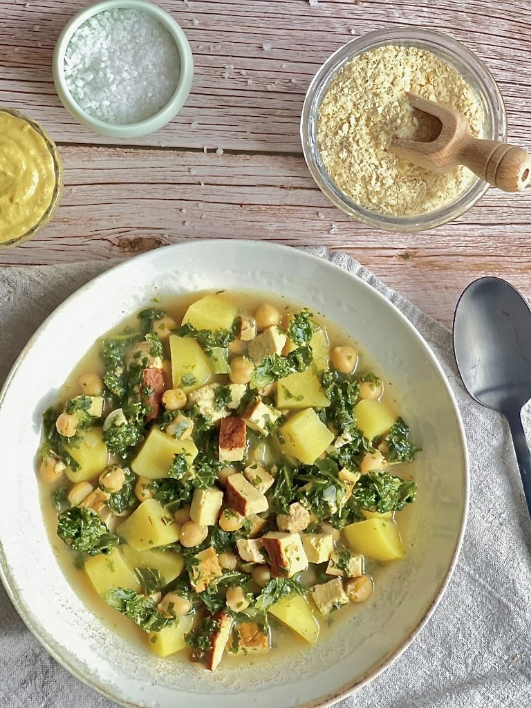 Veganer Kartoffel-Grünkohl-Eintopf mit Räuchertofu und Kichererbsen in einem Suppenteller.