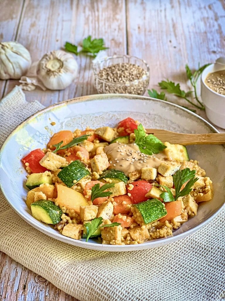 Vegane Hirsepfanne mit Gemüse, Tofu und einer cremigen Tahin-Zitronen-Soße auf einem Teller.