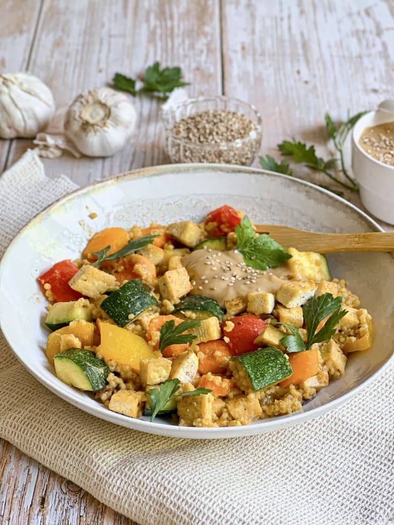 Vegane Hirsepfanne mit Gemüse, Tofu und einer cremigen Tahin-Zitronen-Soße auf einem Teller.