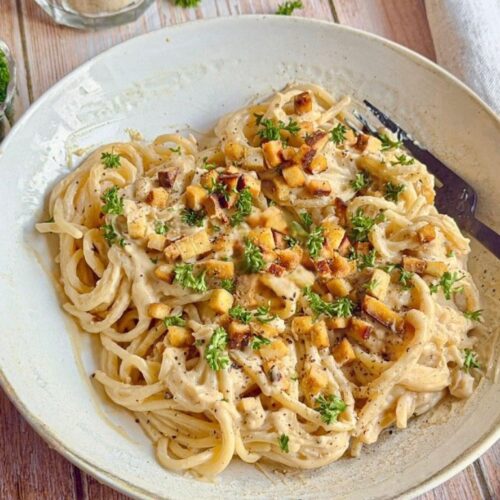 Vegane Spaghetti Carbonara mit Petersilie auf einem Teller.