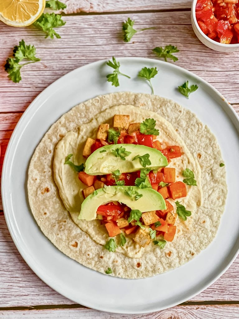 Vegane Wraps mit Süßkartoffelln, Tofu, Hummus, Tomatensalsa und Avocado auf einem Teller.