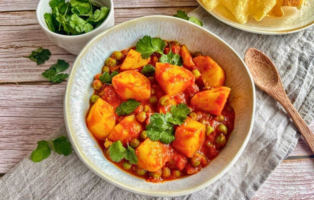 Aloo Matar: Ein herzhaftes indisches Curry mit Kartoffeln und Erbsen auf einem Teller mit Naan-Brot.