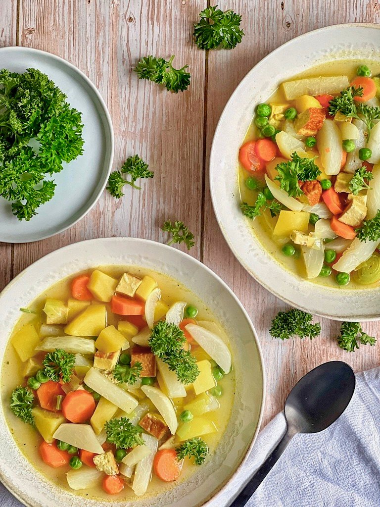 Leckerer veganer Mairübchen-Eintopf mit Gemüse, Kartoffeln, Räuchertofu und Petersilie in Suppentellern.