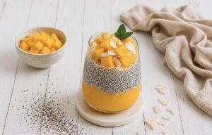 Mango-Chiapudding mit Kokos im Glas auf einem Holztisch.