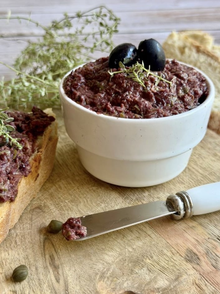 Vegane Oliventapenade auf einem Holzbrett.