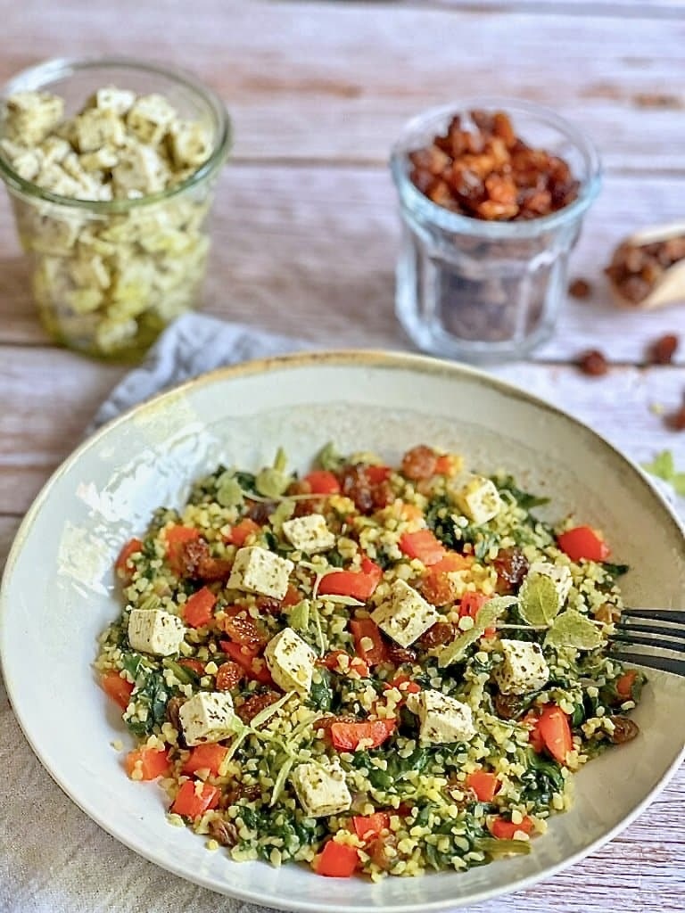 Vegane Bulgurpfanne mit Spinat, Paprika, Rosinen und Kräutertofu auf einem Teller platziert.