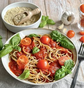 Vegane Tomaten Basilikum Pasta auf einem Teller mit Cashew-Parmesan in einer Schüssel.