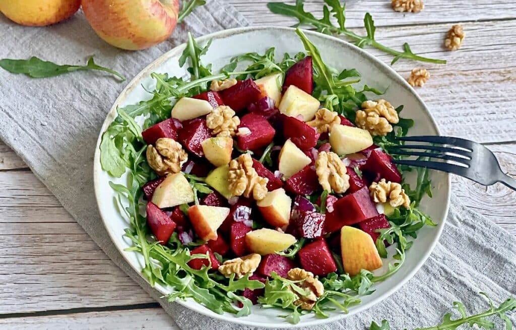 Rote-Bete-Salat mit Apfel, Rucola und Walnüssen auf einem Teller.