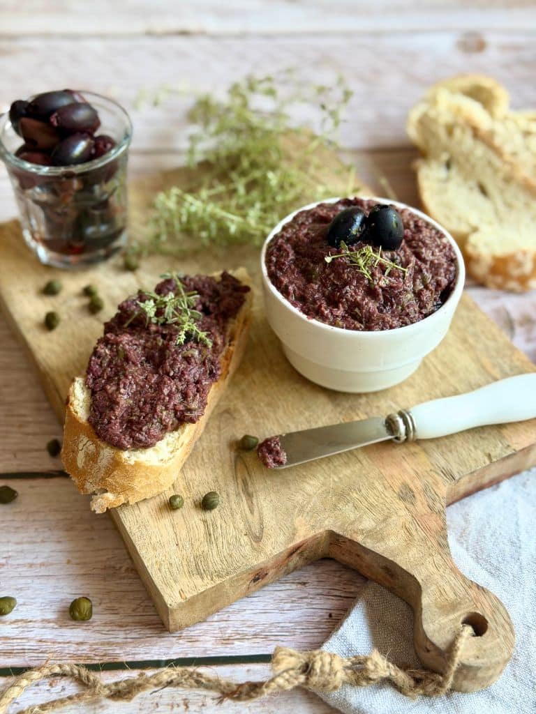 Veganer Olivenaufstrich in einer kleinen Schüssel auf einem Holzbrett.
