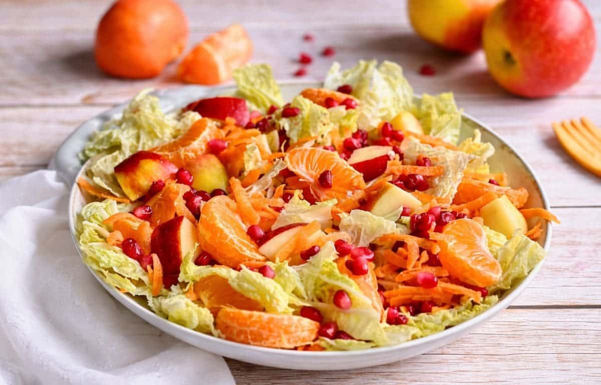 Chinakohlsalat mit Mandarinen, Äpfeln, Karotten und Granatapfelkernen in einer Schüssel